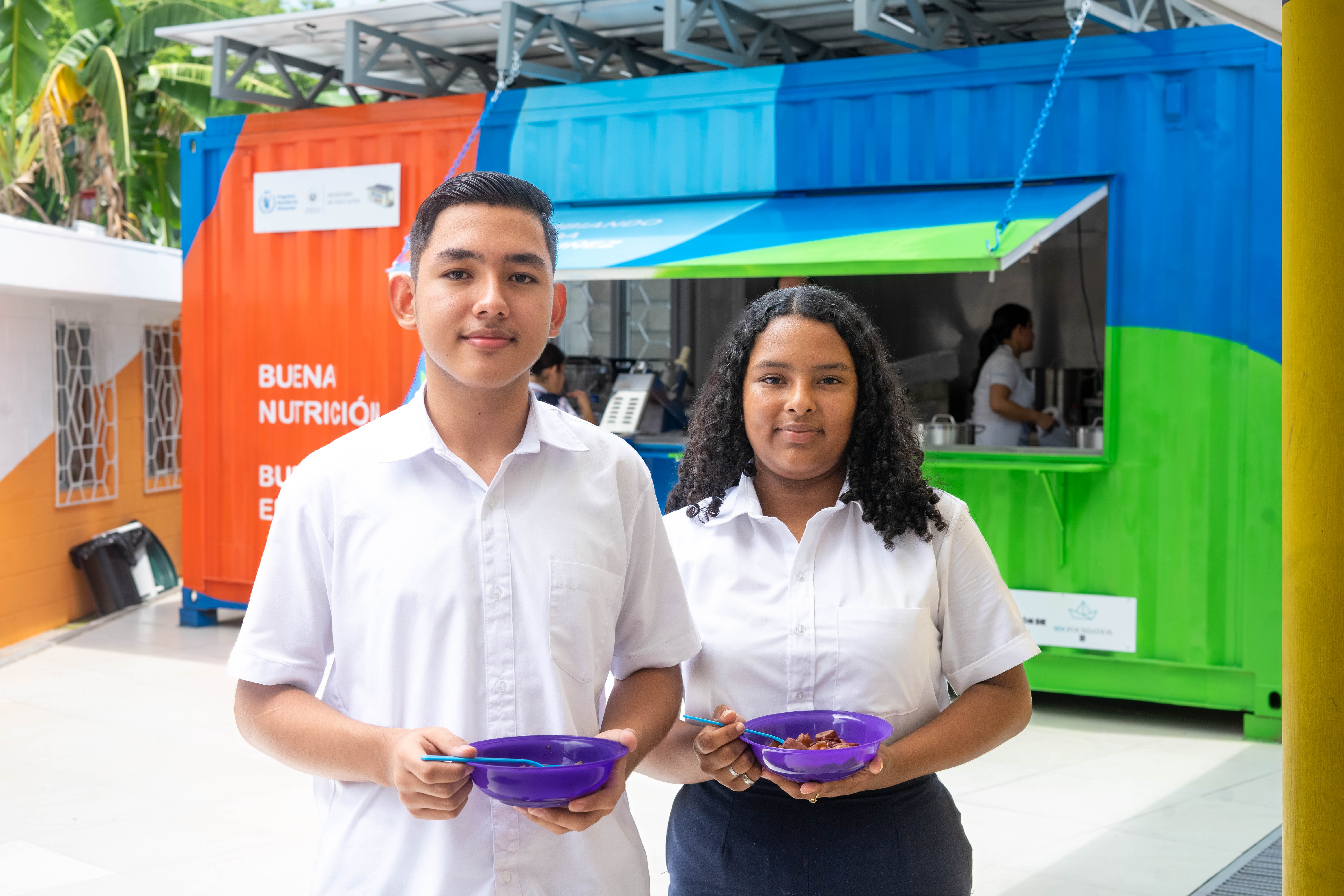 Two children smiling to camera with their meal provided by Kitchen-In-A-Box.